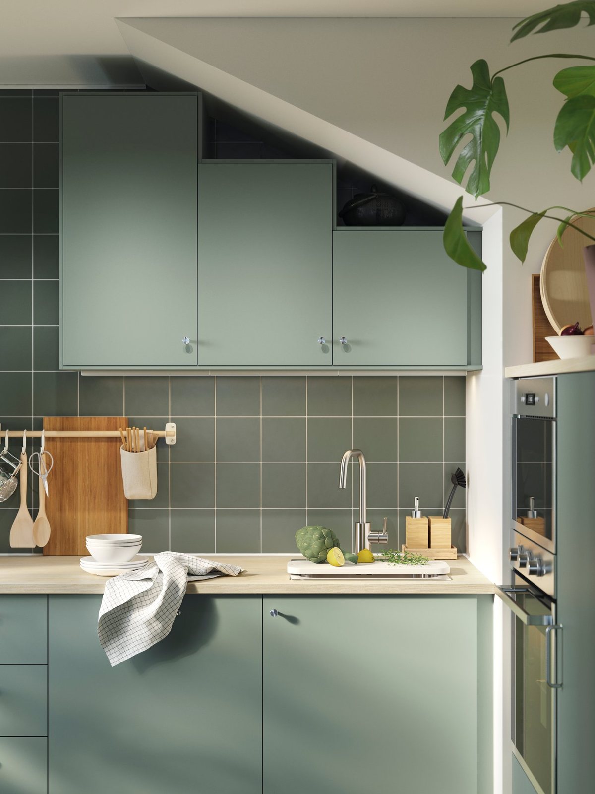 A fitted kitchen with grey-green cabinet fronts, a pale worktop and a tiled wall