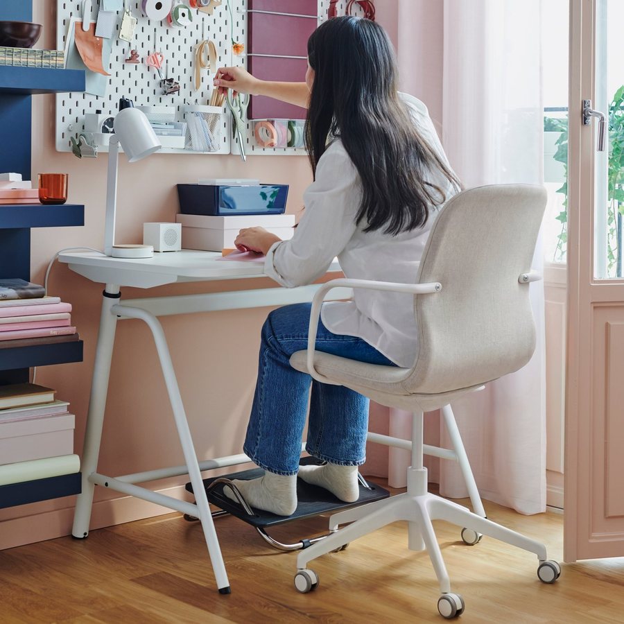 A person working at a white desk by a window, on an upholstered task chair
