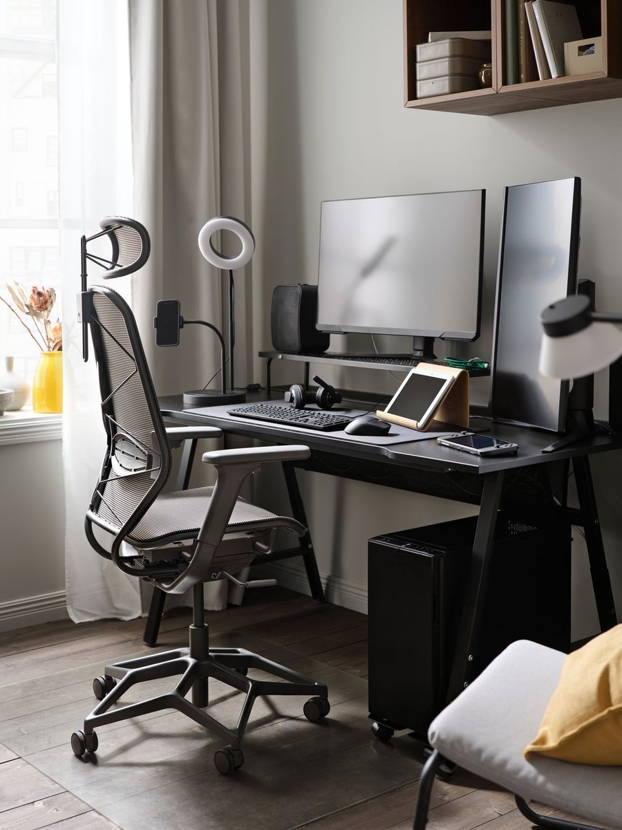 A home workspace with a desk, monitor arm and a task chair beside a window