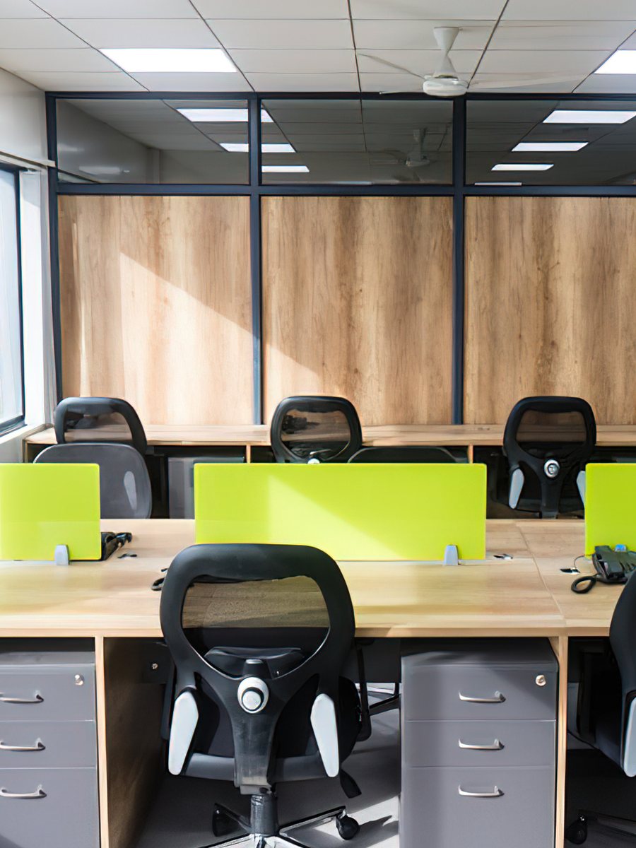 An open-plan office Woodware furnished — rows of desks with green screens and black task chairs beside a window wall